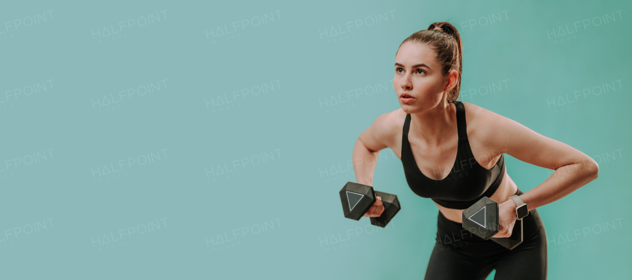 An athletic fitness woman working out with dumbbells on green background. Copy space.