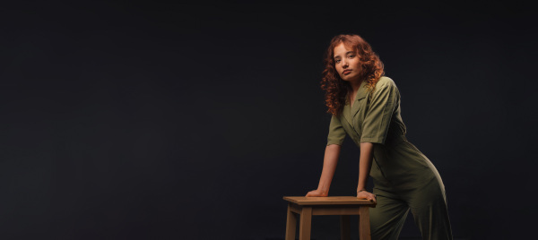 Portrait of a young redhead woman leaning on bar chair, studio shoot.