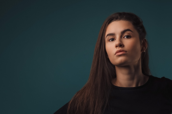 Portrait of a young woman in studio, dark blue background.