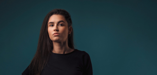 Portrait of a young woman in studio, dark blue background.