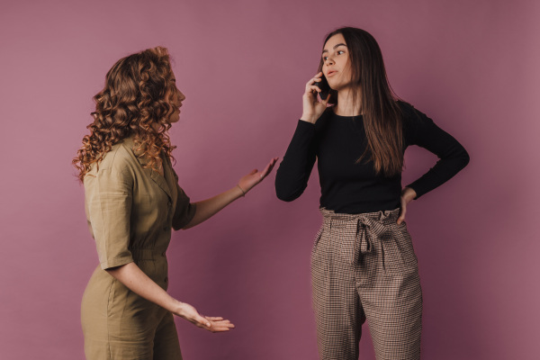 Studio shoot of two young women, one has long call with a mobile phone.