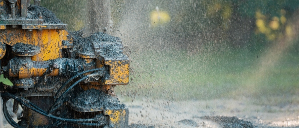 Close up of well drilling rig boring dowin into the earth. A rotary drill rig using bits to bore into ground and loosing the soil and rocks. Drilling machine, equipment using water to cool down bits. Mud and muddy water is spitting out when drilling borewell. Banner with copy space.