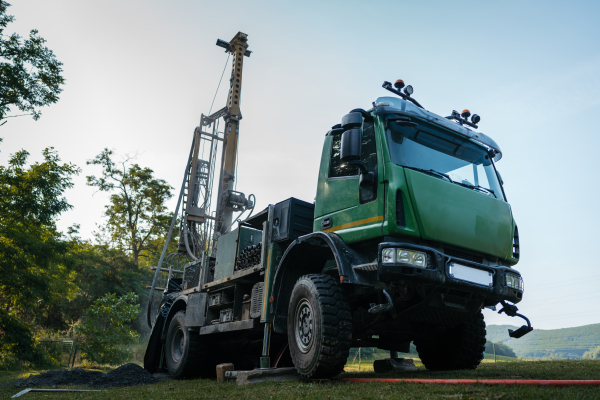 Water well drilling rig, truck preparing to boring dowin into the earth. A rotary drill rig using bits to bore into ground and loosing the soil and rocks. Drilling machine, equipment using water to cool down bits. Mud and muddy water is spitting out when drilling borewell. Banner with copy space.