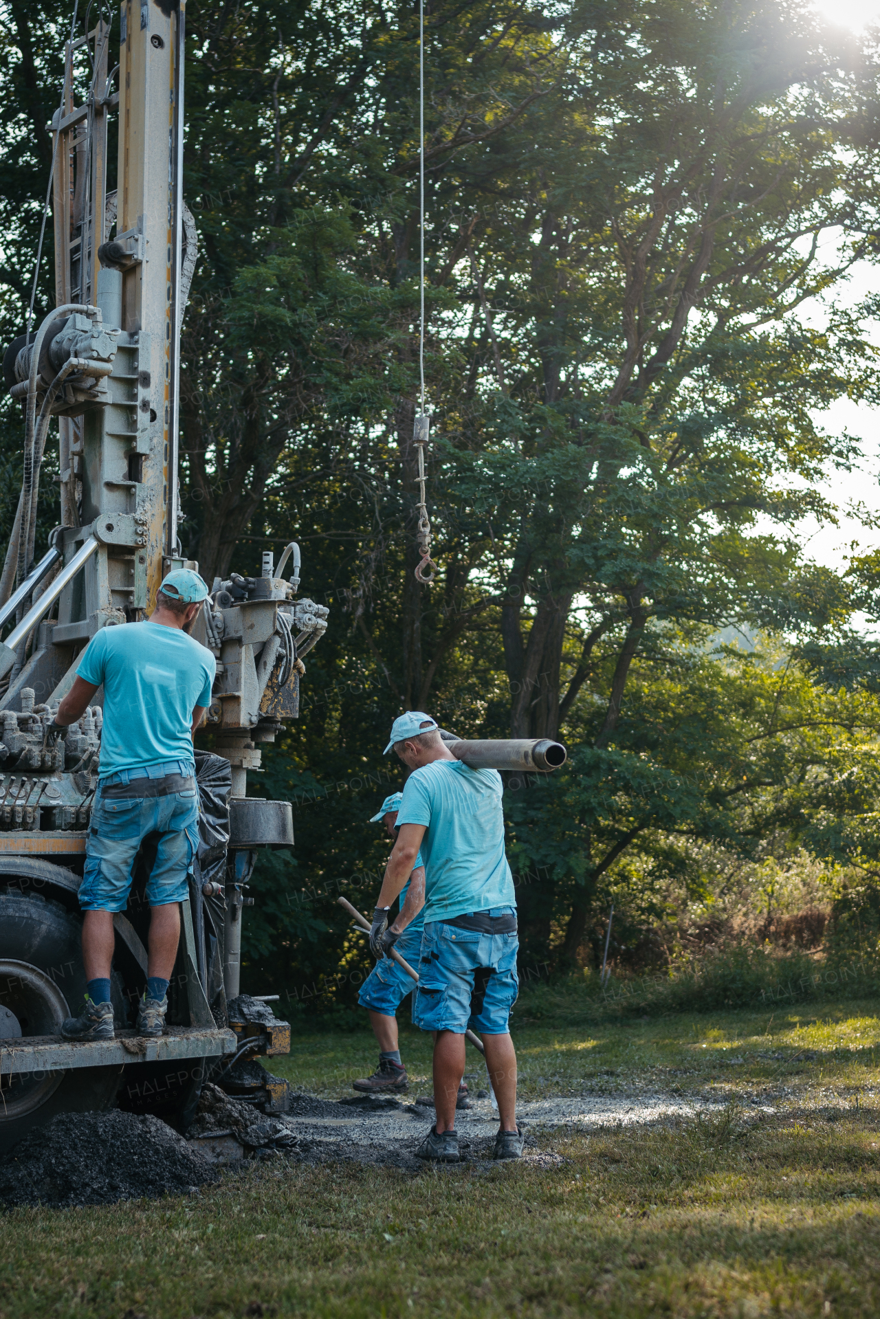 Water well drilling rig, truck preparing to boring dowin into the earth. Professional workers operating drilling machine, equipment. A rotary drill rig using bits to bore into ground and loosing the soil and rocks. Mud and muddy water is spitting out when drilling borewell. Banner with copy space.