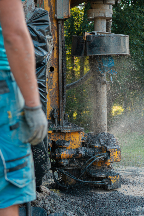 Close up of well drilling rig boring dowin into the earth. A rotary drill rig using bits to bore into ground and loosing the soil and rocks. Drilling equipment using water to cool down bits. Professional worker looking at working machine. Mud and muddy water is spitting out when drilling borewell. Banner with copy space.