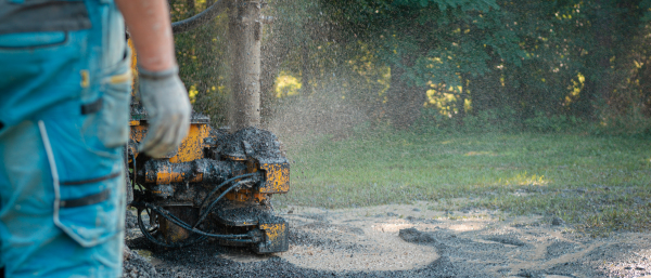 Close up of well drilling rig boring dowin into the earth. A rotary drill rig using bits to bore into ground and loosing the soil and rocks. Drilling equipment using water to cool down bits. Professional worker looking at working machine. Mud and muddy water is spitting out when drilling borewell. Banner with copy space.