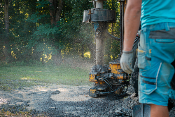 Close up of well drilling rig boring dowin into the earth. A rotary drill rig using bits to bore into ground and loosing the soil and rocks. Drilling equipment using water to cool down bits. Professional worker looking at working machine. Mud and muddy water is spitting out when drilling borewell. Banner with copy space.