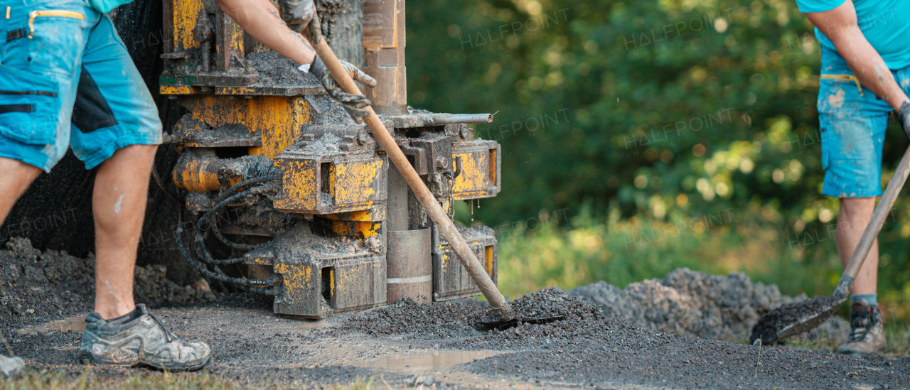 Water well drilling rig, truck preparing to boring dowin into the earth. Professional workers operating drilling machine, shoveling rubble. A rotary drill rig using bits to bore into ground and loosing the soil and rocks. Mud and muddy water is spitting out when drilling borewell. Banner with copy space.