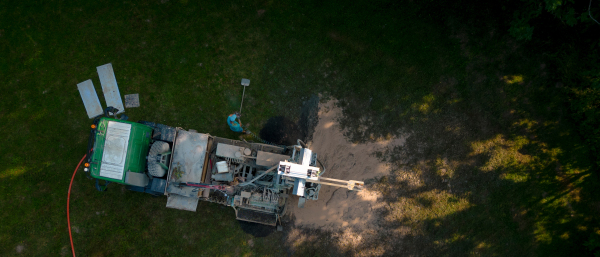 Aerial shot of water well drilling rig boring dowin into the earth. A rotary drill rig using bits to bore into ground and loosing the soil and rocks. Drilling machine, equipment using water to cool down bits. Mud and muddy water is spitting out when drilling borewell. Banner with copy space.