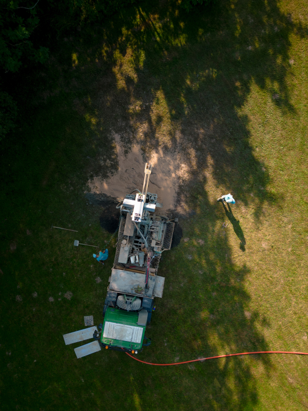 Aerial shot of water well drilling rig boring dowin into the earth. A rotary drill rig using bits to bore into ground and loosing the soil and rocks. Drilling machine, equipment using water to cool down bits. Mud and muddy water is spitting out when drilling borewell. Banner with copy space.