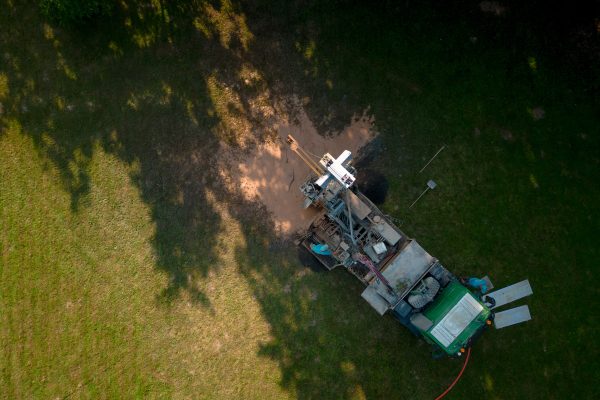 Aerial shot of water well drilling rig boring dowin into the earth. A rotary drill rig using bits to bore into ground and loosing the soil and rocks. Drilling machine, equipment using water to cool down bits. Mud and muddy water is spitting out when drilling borewell. Banner with copy space.