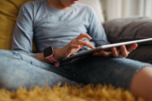 Cute girl spending free time indoors, scrolling on tablet. Using social media and smartwatch.