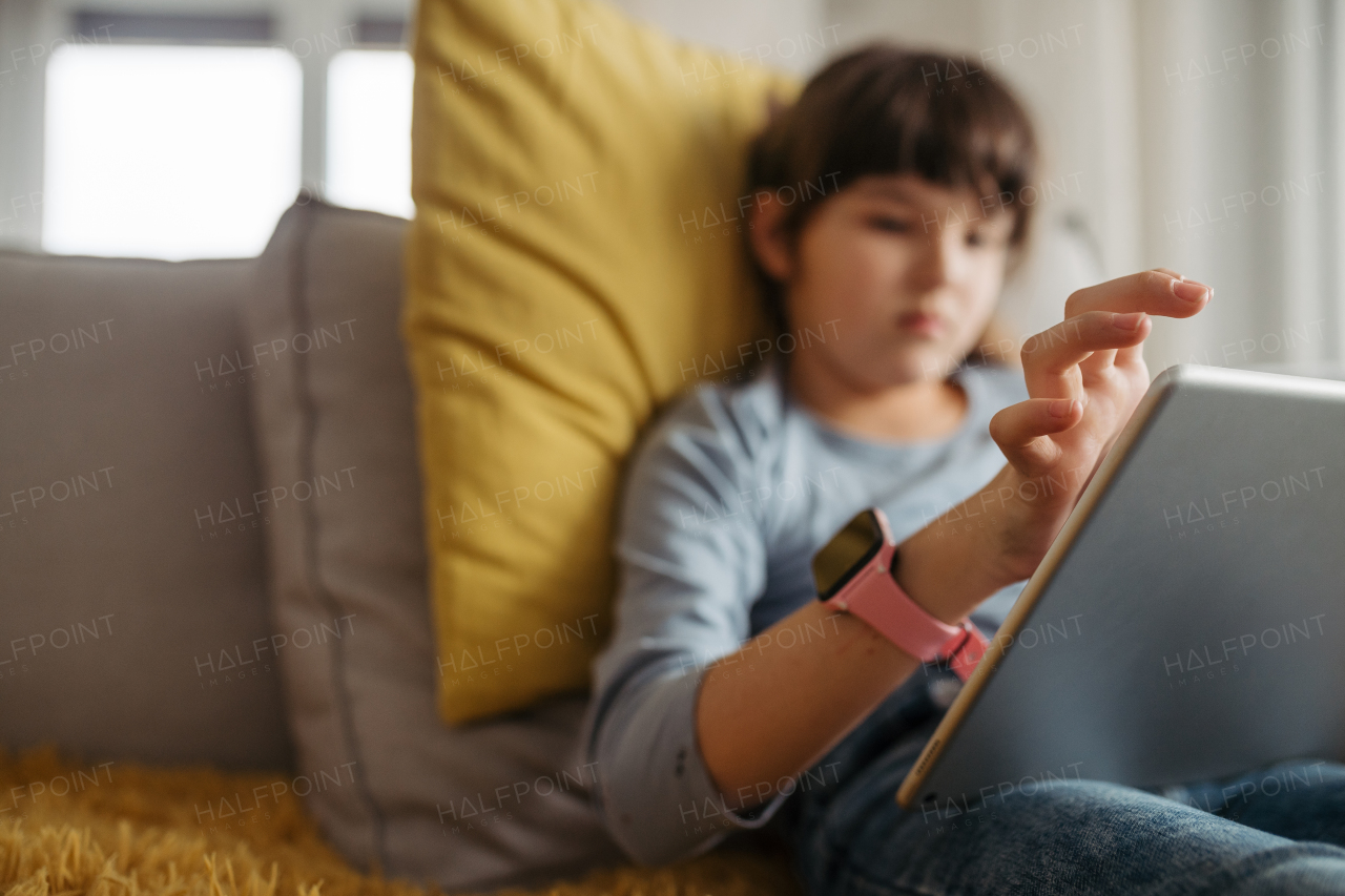 Cute girl spending free time indoors, scrolling on tablet. Using social media and smartwatch.