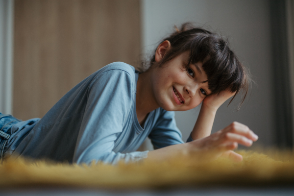 Cute girl lying on belly on the floor, scrolling on smartphone. Using social media. Side view.