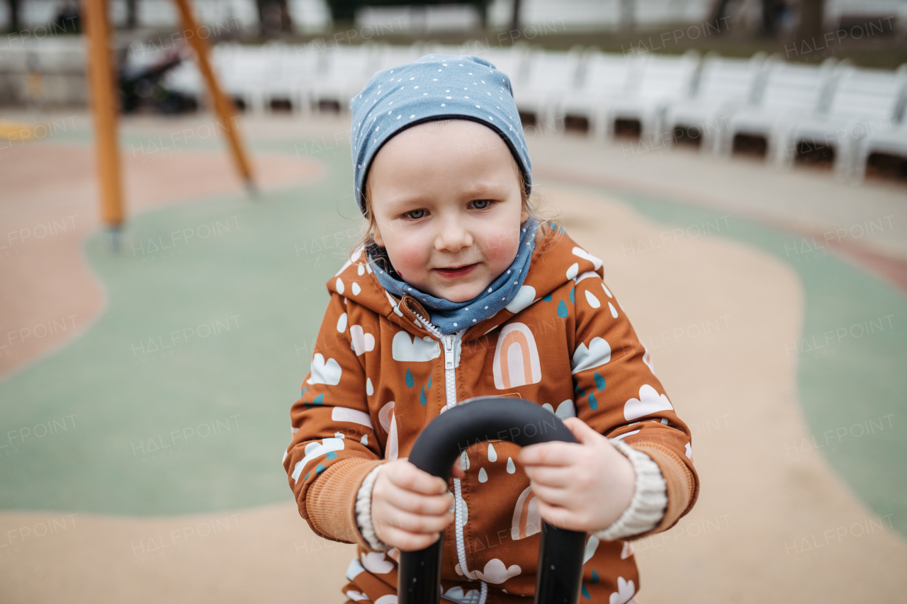 Cute toddler girl playing outdoor in playground. Girl in softshell bodysuit spending time in city park.