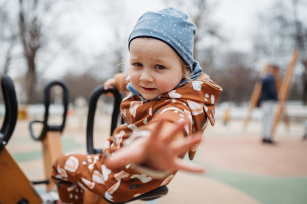 Cute toddler girl playing outdoor in public park playground. Girl in softshell bodysuit spending time in city park.