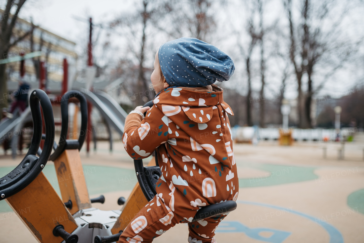 Cute toddler girl playing outdoor in playground, on urban gym. Girl in softshell bodysuit spending time in city park.