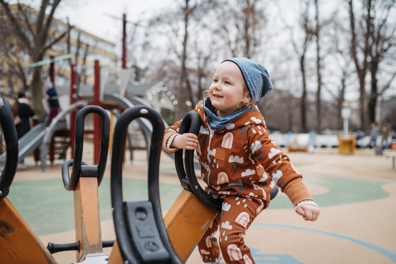 Cute toddler girl playing outdoor in public park playground. Girl in softshell bodysuit spending time in city park.