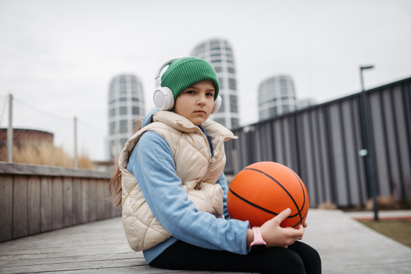 Sad girl alone in the city, want to play basketball. Young girl spending free time alone in the city, no friends, no activity. Mental health problems.