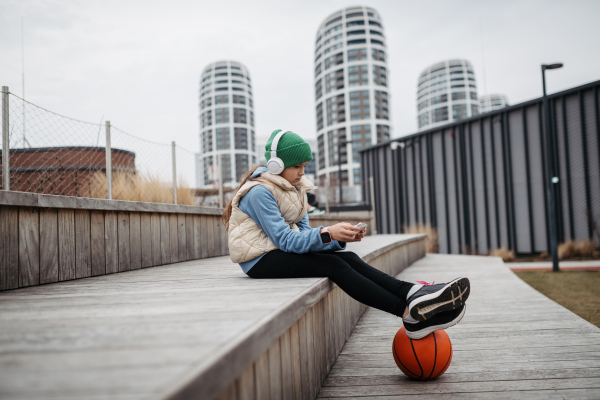 Girl sitting on city public playground, scrolling on smartphone. Using social media. Online bullying or cyberbullying for a young schoolgirl.