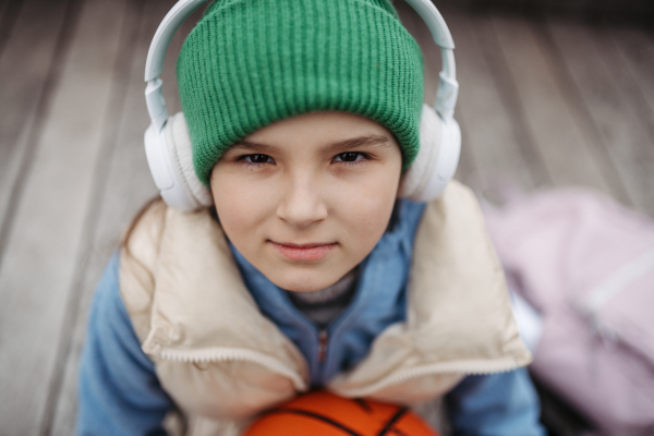 Outdoor portrait of cute young girl with beanie and headphones. Girl with a long hair standing on playground in the city.