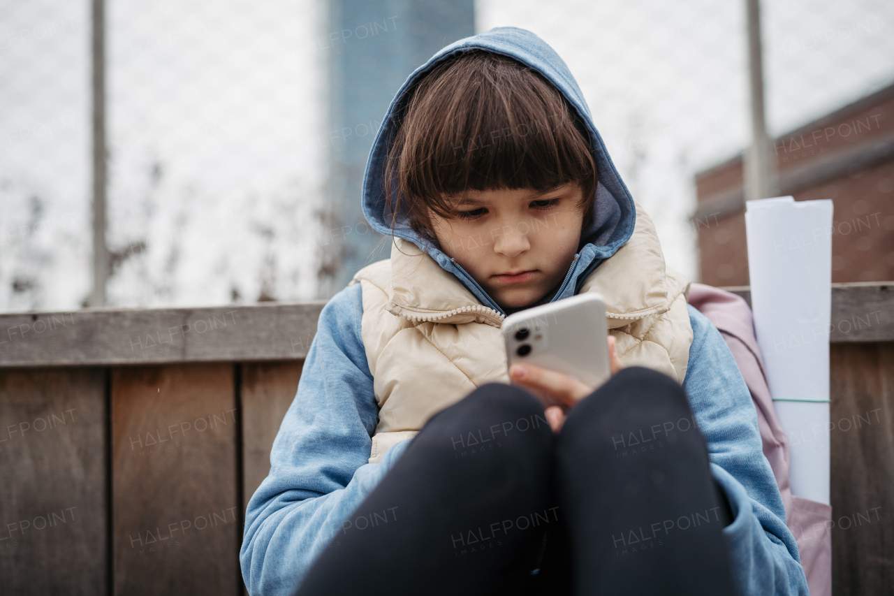 Girl sitting in front of school building, scrolling on tablet. Using social media. Online bullying or cyberbullying for a young schoolgirl.