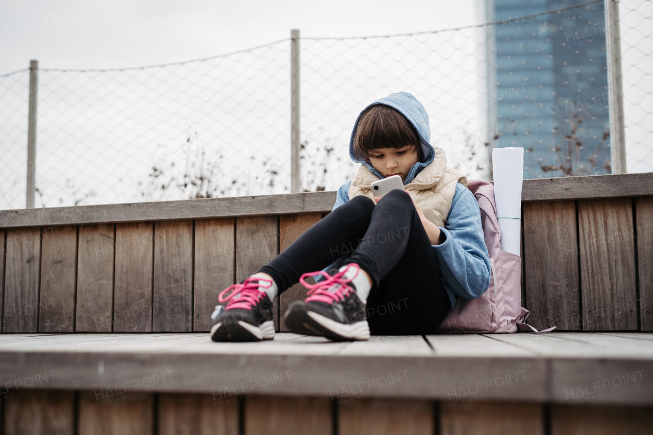 Sad girl phone calling, sitting in front of school building, waiting for parents. Young schoolgirl with no friends, feeling lonely. Mental health problems.