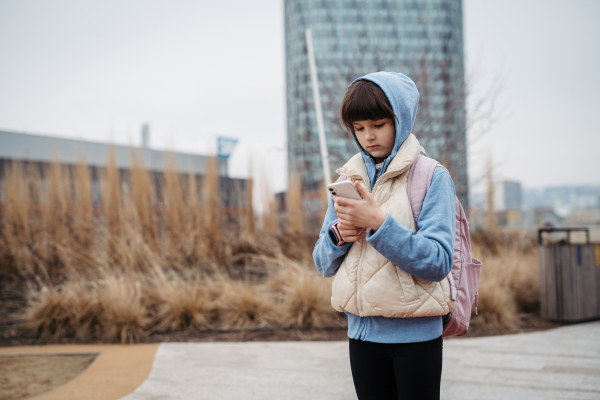 Girl standing outdoors, scrolling on the smartphone. Using social media. Online bullying or cyberbullying for young schoolgirl.