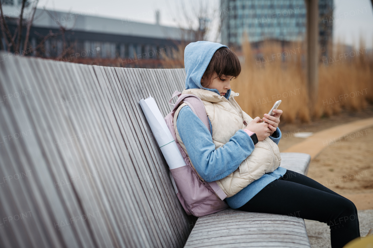 Girl in front of school building, scrolling on smartphone. Using social media. Online bullying or cyberbullying for a young schoolgirl.