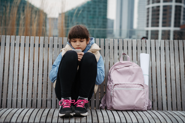 Girl sitting in front of school building, scrolling on tablet. Using social media. Online bullying or cyberbullying for a young schoolgirl.