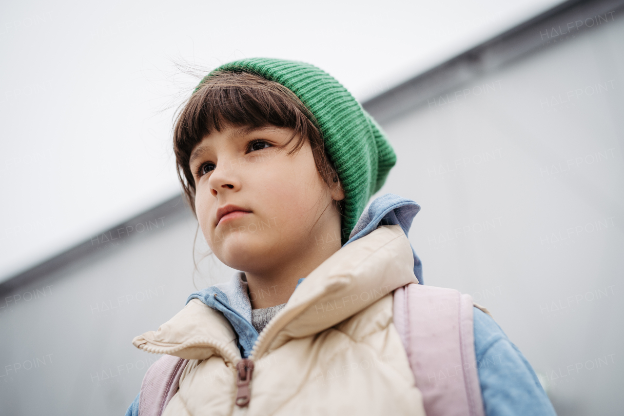 Outdoor portrait of cute young girl with beanie hat, laughing. Girl with a long hair standing on playground in the city.