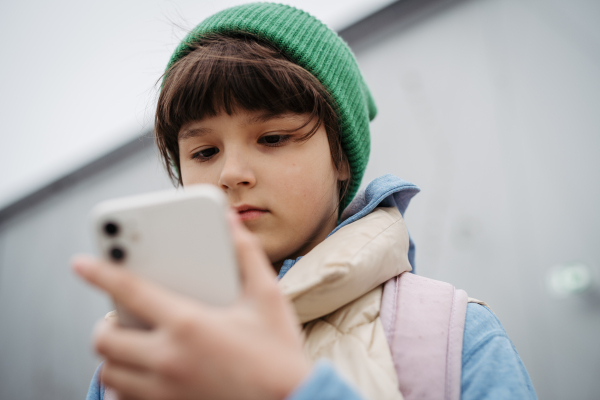 Girl standing outdoors, scrolling on the smartphone. Using social media. Online bullying or cyberbullying for young schoolgirl.