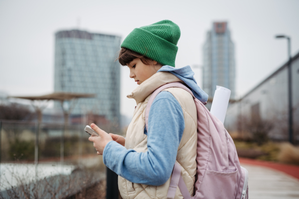 Girl in front of school building, scrolling on tablet. Using social media. Online bullying or cyberbullying for a young schoolgirl.