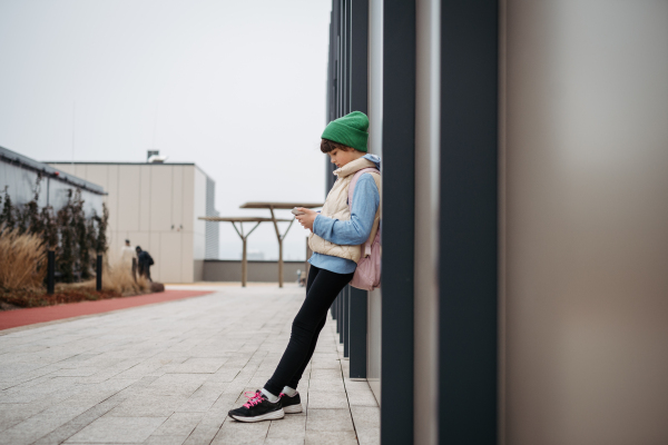 Girl standing outdoors, scrolling on the smartphone. Using social media. Online bullying or cyberbullying for young schoolgirl.