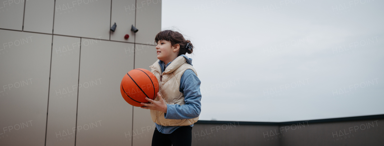 Girl in the city playing basketball. Young girl spending a free time doing sport, enjoying after schoold outdoor activity. Banner with copy space.