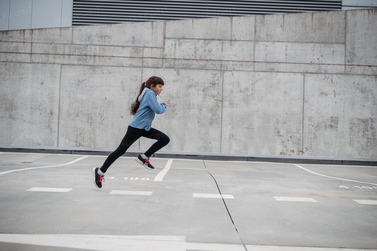 Girl in the city running, doing sport. Young girl spending free time exercising, enjoying after school outdoor activity.