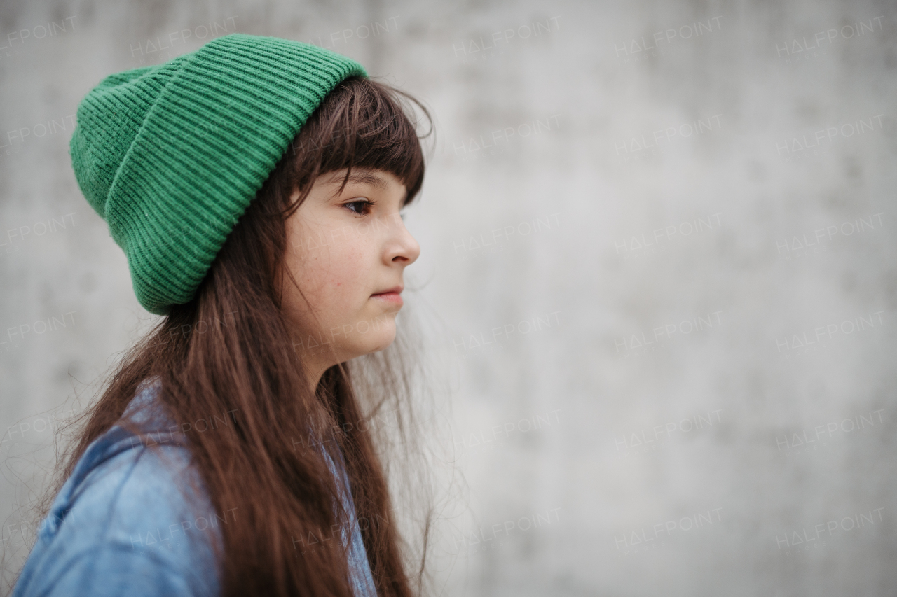 Side view portrait of cute young girl with beanie hat, laughing. Girl with a long hair standing on playground in the city.