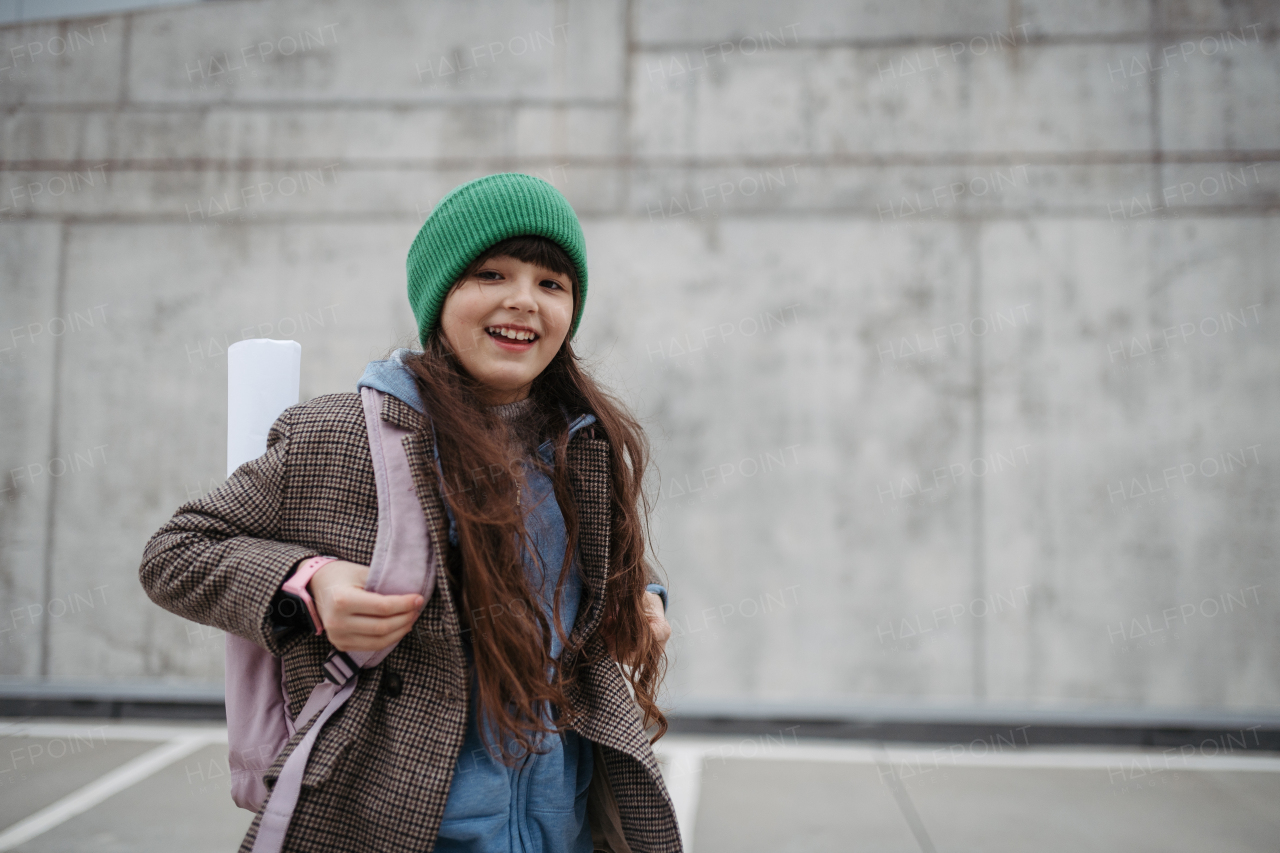 Outdoor portrait of cute young girl with beanie hat, laughing. Girl with a long hair standing on playground in the city.