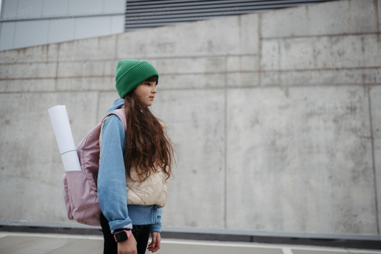 Outdoor portrait of sad young girl with beanie hat and backpack. Girl with long hair going to school, feeling anxious, depressed.