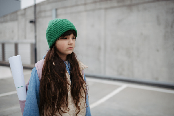 Outdoor portrait of sad young girl with beanie hat and backpack. Girl with long hair going to school, feeling anxious, depressed.