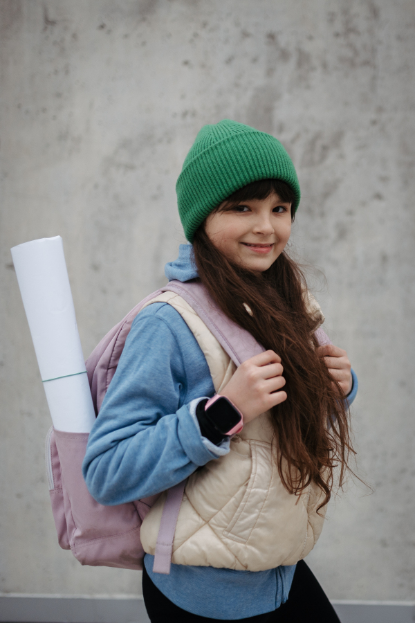 Outdoor portrait of cute young girl with beanie. Girl with a long hair standing on playground in the city.