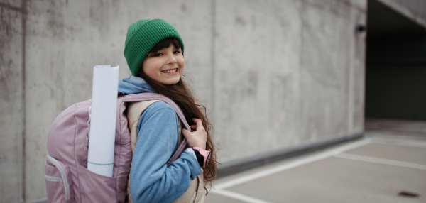 Outdoor portrait of cute young girl with beanie hat, laughing. Girl with a long hair standing on playground in the city. Banner with copy space.