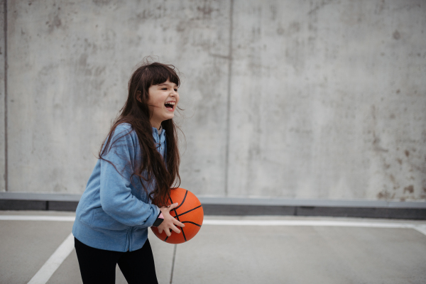 Girl in the city playing basketball. Young girl spending a free time doing sport, enjoying after schoold outdoor activity.