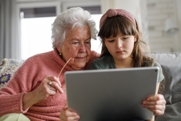 Grandmother with cute girl scrolling on tablet, girl teaching senior woman to work with technology, internet. Portrait of an elderly woman spending time with granddaughter.