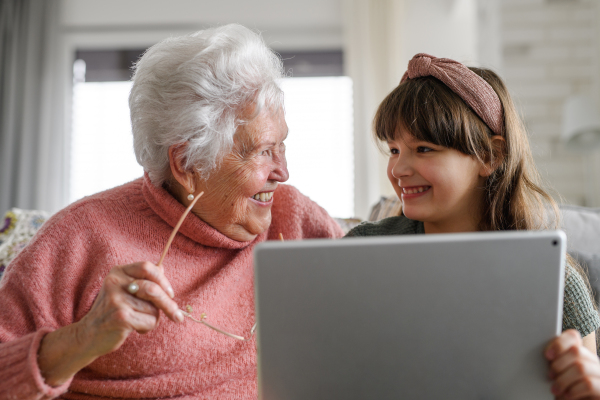 Grandmother with cute girl scrolling on tablet, girl teaching senior woman to work with technology, internet. Portrait of an elderly woman spending time with granddaughter.