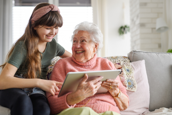 Grandmother with cute girl scrolling on tablet, girl teaching senior woman to work with technology, internet. Portrait of an elderly woman spending time with granddaughter.