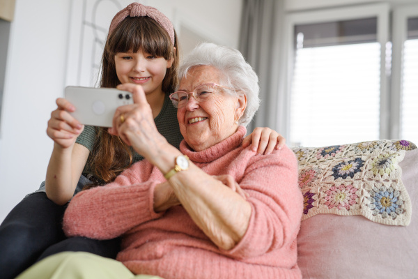 Grandmother with cute girl scrolling on smartphone, girl teaching senior woman to work with technology, internet. Portrait of an elderly woman spending time with granddaughter.