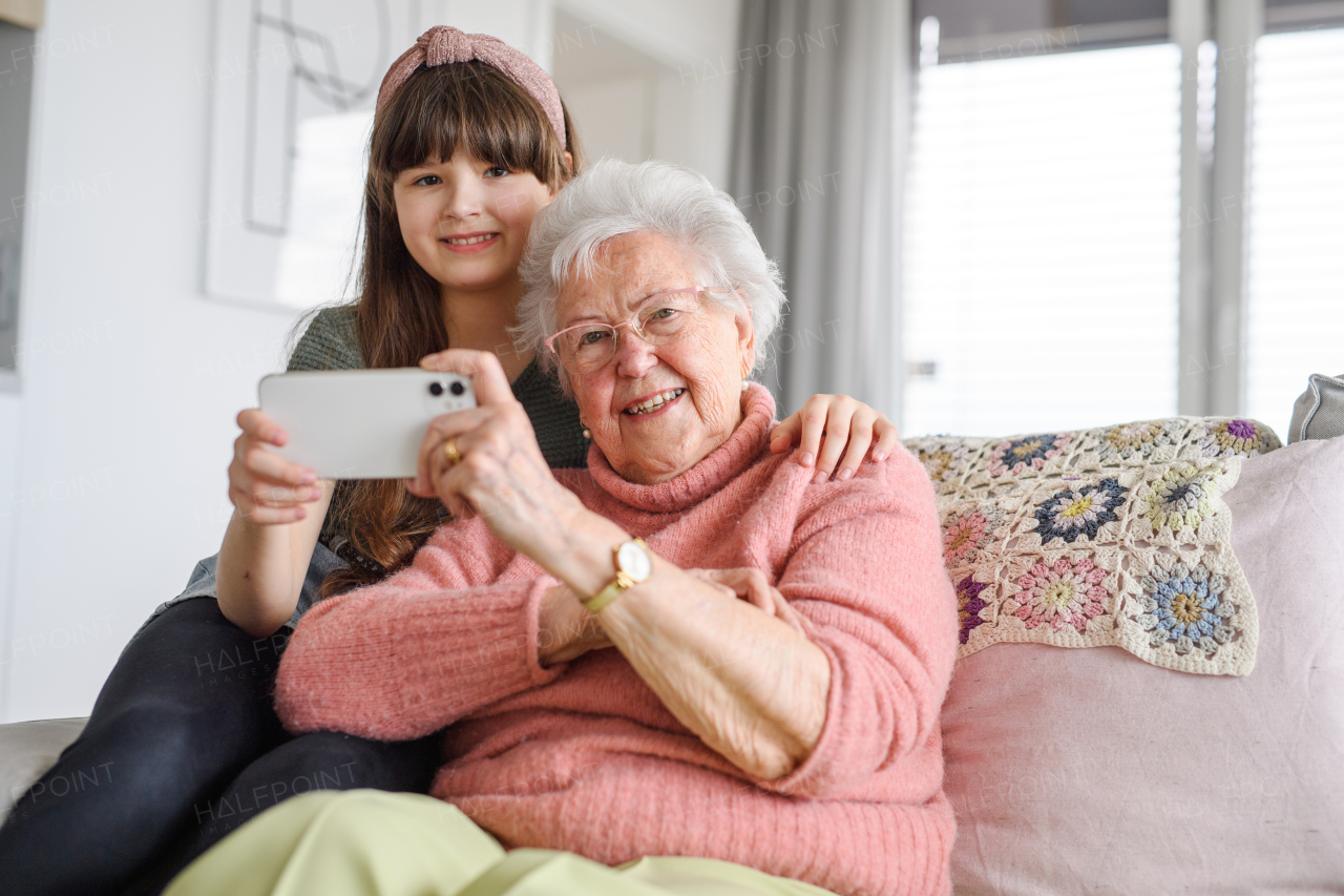 Grandmother with cute girl taking selfie with smartphone. Portrait of an elderly woman spending time with a granddaughter.