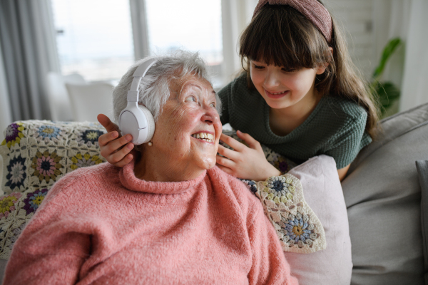 Cute girl putting headphones on gradmother head. Portrait of an elderly woman spending time with a granddaughter.