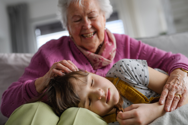 Sleeping girl lying head on gradmother knees, caressing her hair. Portrait of an elderly woman spending time with granddaughter.